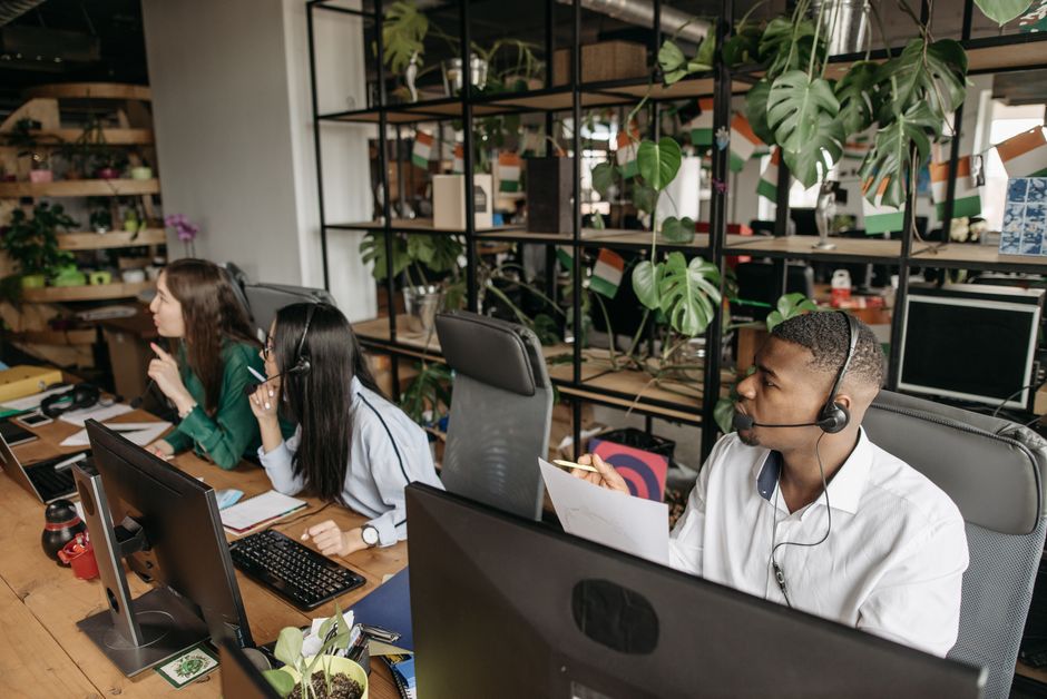 Equipe de atendimento ao cliente em ambiente de escritório colaborativo, utilizando computadores e headsets para suporte remoto.