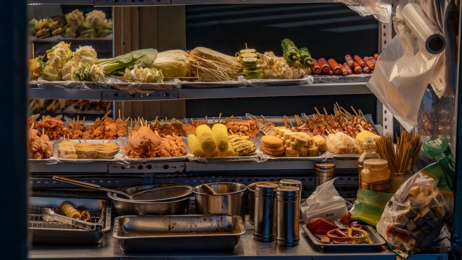 Exposição de ingredientes para churrasco, incluindo carnes, legumes e acompanhamentos, em um açougue ou lanchonete