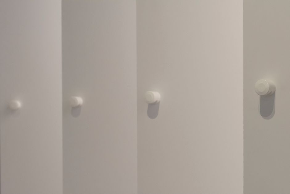 Imagem de cabides brancos fixados em uma parede suave, sugerindo um espaço de armazenamento ou organização de roupas.