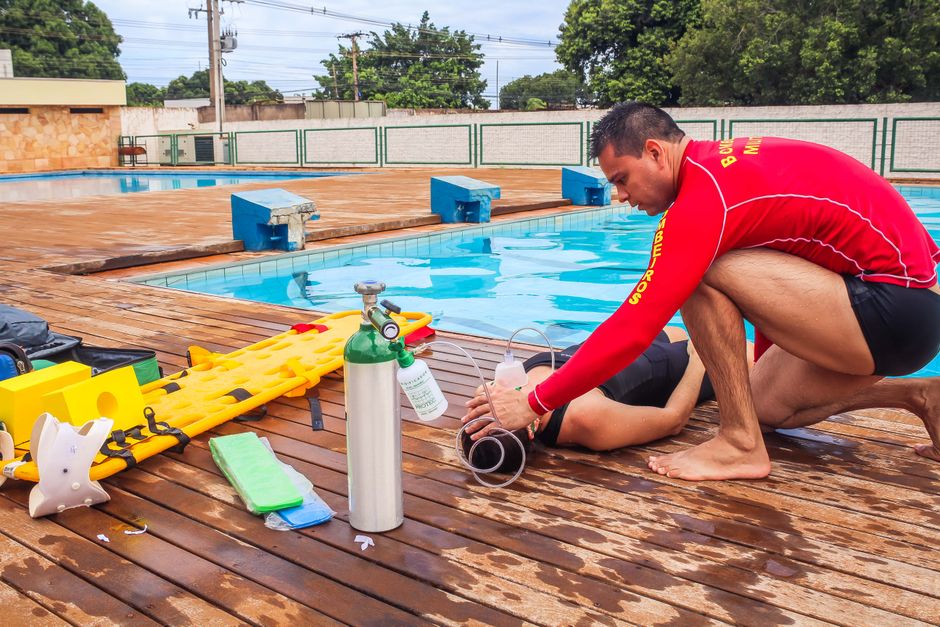 Socorristas realizando treinamento de primeiros socorros ao lado de uma piscina ao ar livre.