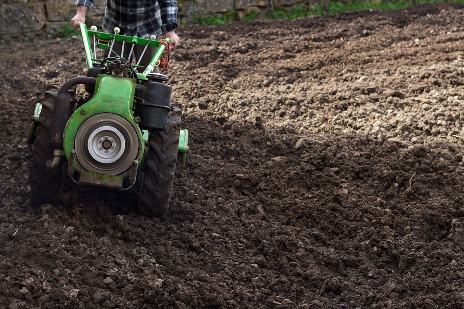 Pessoa utilizando uma cultivadora de solo em um campo preparado para plantio, destacando práticas agrícolas sustentáveis.