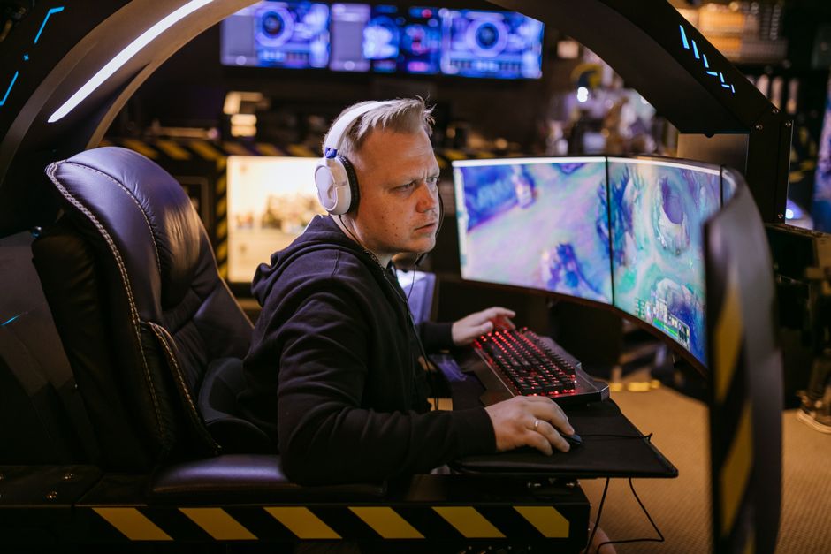 Homem jogando videogame em um ambiente de entretenimento com várias telas de alta tecnologia.