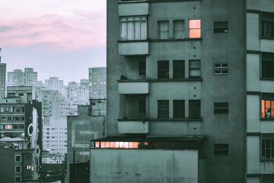 Imagem de um edifício residencial em um cenário urbano ao entardecer, com janelas iluminadas criando um contraste visual na fachada.