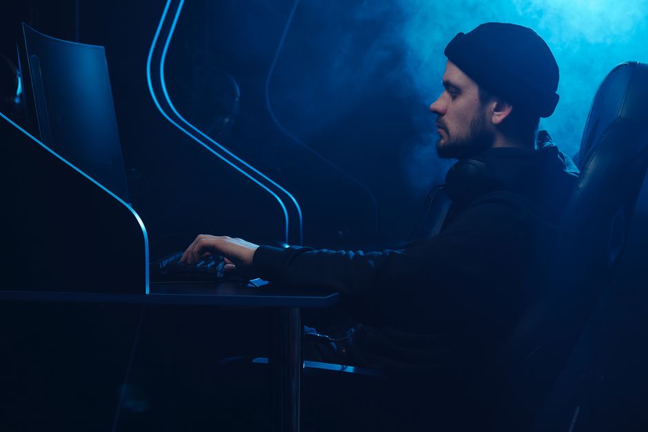 Homem jogando videogame com foco, em ambiente com iluminação azul e atmosfera futurista.