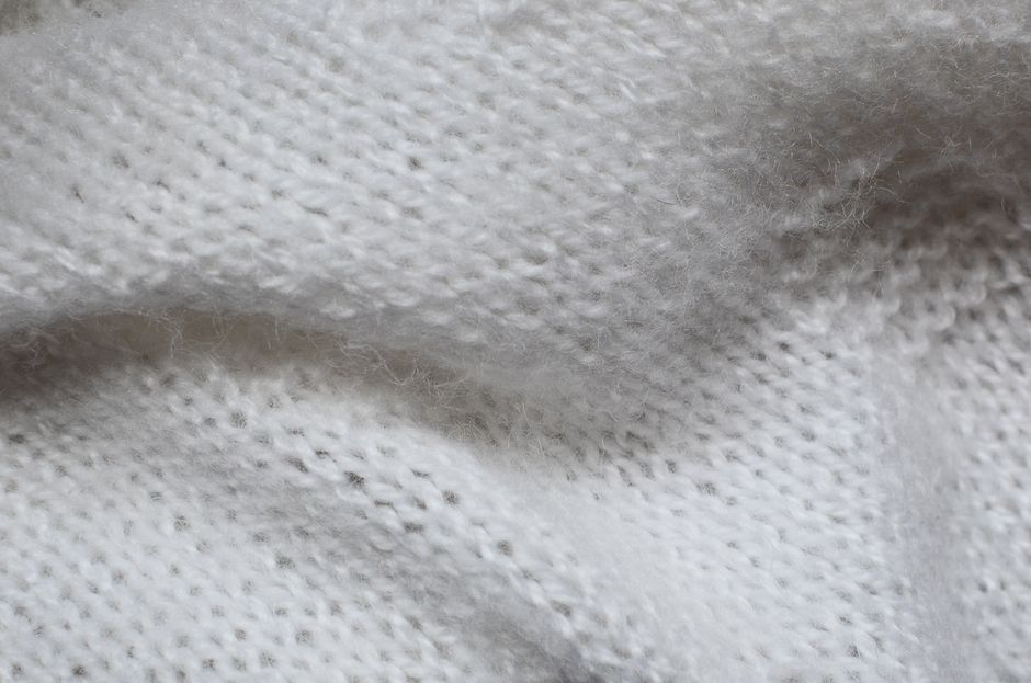 Imagem de uma peça de tecido branco com textura macia e detalhes em ponto de tricô ou crochê, sugerindo conforto ou moda.