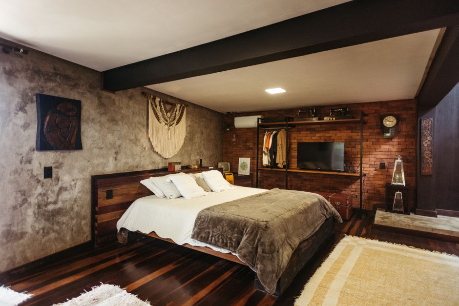 Quarto moderno com detalhes de design rústico, destaque para a parede de tijolos e iluminação aconchegante.