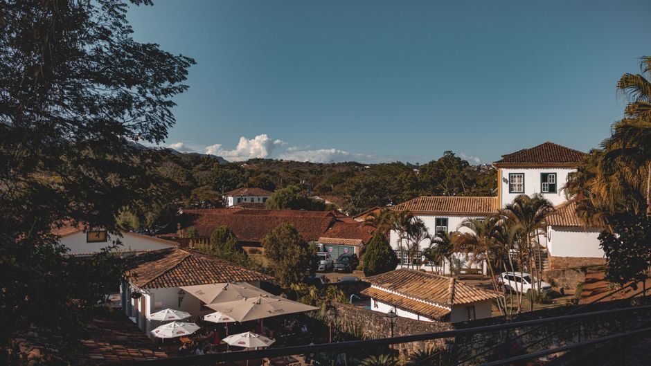 Visão panorâmica de uma vila com casas de arquitetura colonial espanhola, predominantemente brancas com telhados de cerâmica, cercada por vegetação tropical e com um céu claro ao fundo.