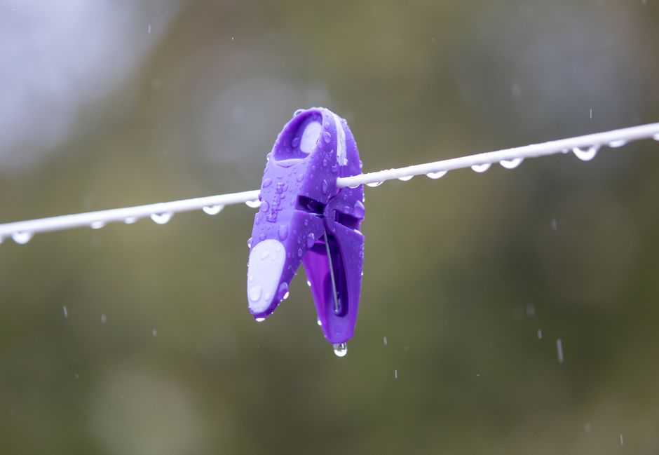 Clipping de uma roupa pendurada em um varal após a chuva, com gotas de água visíveis na peça e na linha de costura.