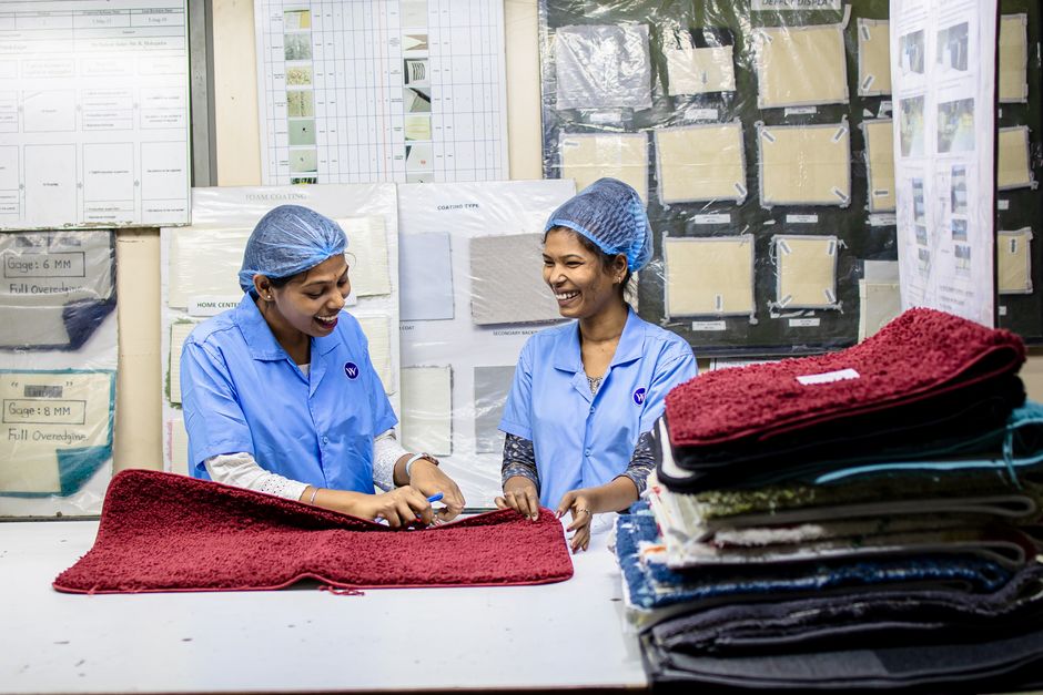 Duas funcionárias de uma fábrica de tecidos trabalham juntas na conferência de uma toalha de roupa, destacando o ambiente de produção têxtil e controle de qualidade.