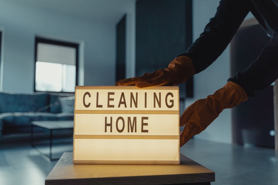 Pessoa colocando uma placa com a mensagem 'Cleaning Home', simbolizando serviços de limpeza residencial ou manutenção doméstica.