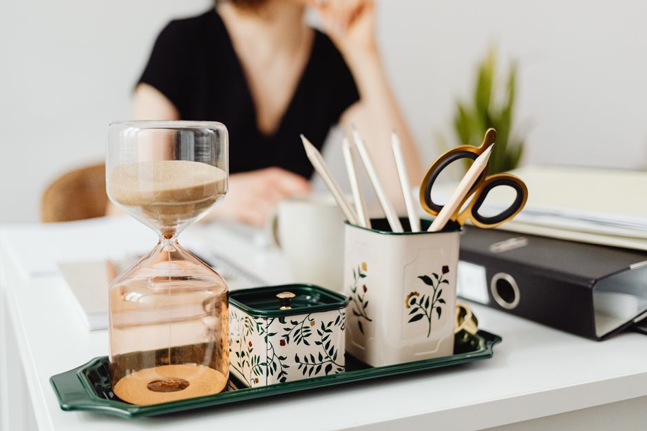 Imagem de um ambiente de trabalho com objetos de escritório e uma pessoa ao fundo, sugerindo produtividade e organização.