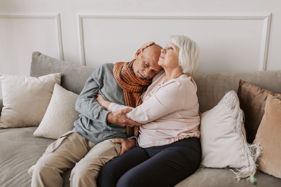 Imagem emocionante de um casal idoso compartilhando um momento de afeto e carinho no sofá de casa.