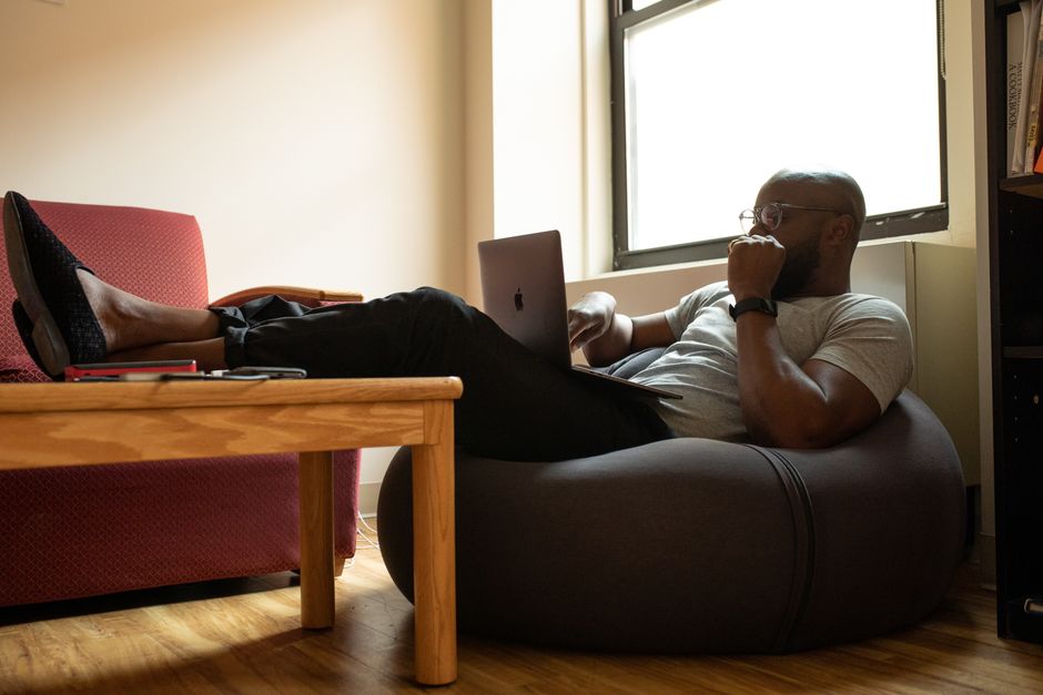 Homem relaxando em ambiente de trabalho informal enquanto usa o laptop, refletindo uma abordagem moderna e confortável para o trabalho remoto.