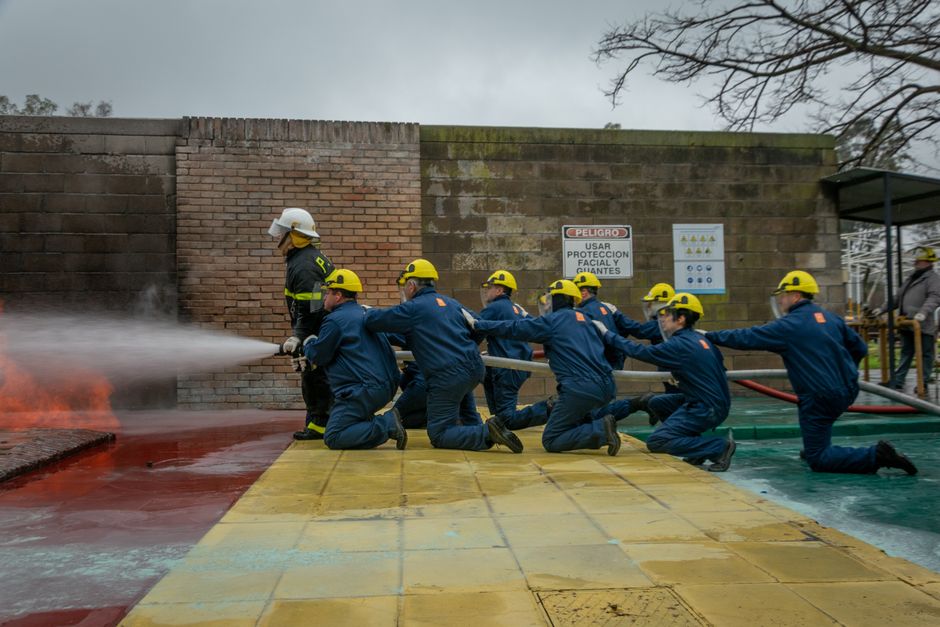 Equipe de bombeiros treinando para controlar incêndios em ambiente industrial.