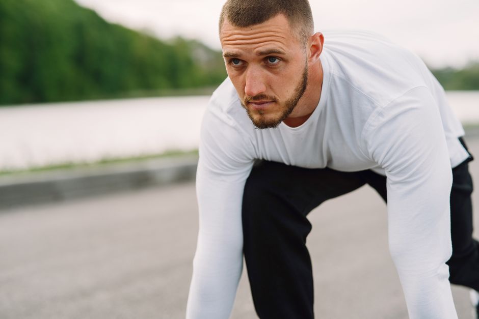 Homem preparado para corrida ou atividade física ao ar livre, focado no início do exercício.
