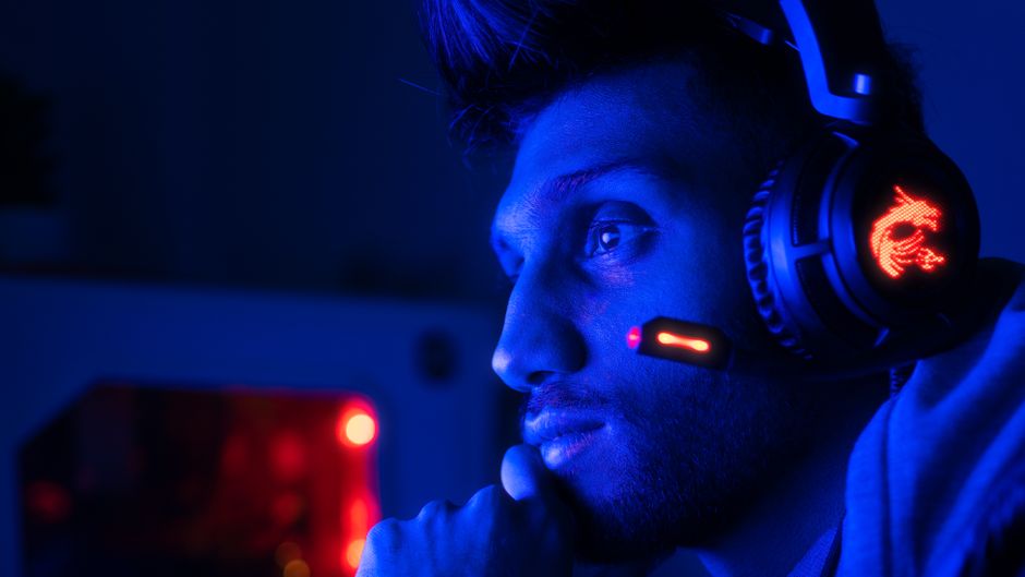 Pessoa concentrada jogando videogame em ambiente com iluminação azul e iluminação de LED, destacando o foco no entretenimento digital.