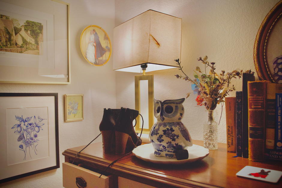 Um canto aconchegante decorado com livros, uma luminária, uma planta e uma decoração de chá de presentão, transmitindo conforto e personalidade em um espaço residencial.
