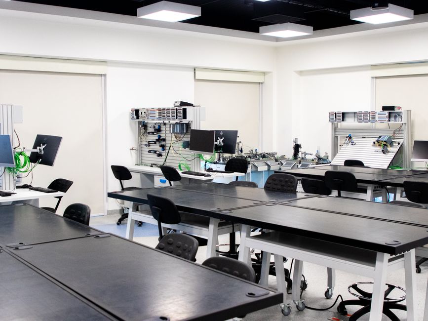 Laboratório de tecnologia ou inovação com mesas de trabalho e equipamentos eletrônicos em ambiente moderno e bem iluminado.