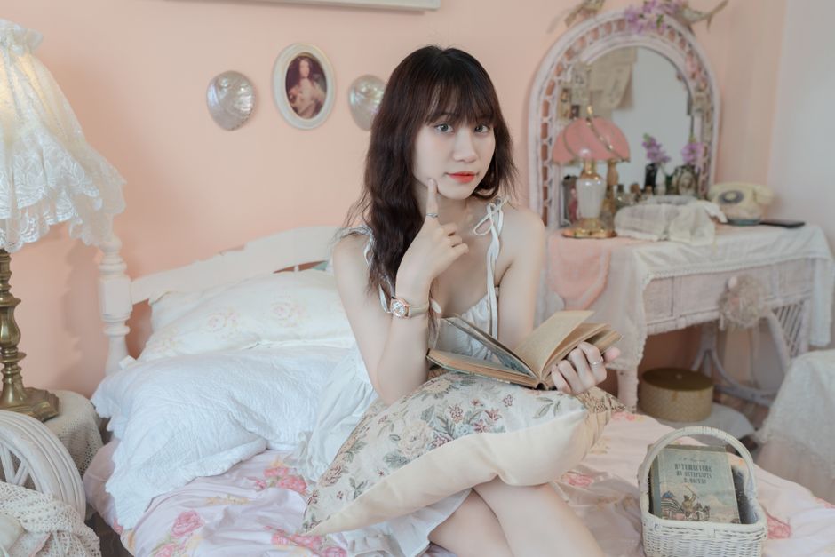 Mulher jovem lendo um livro em um ambiente decorado de forma delicada e feminina, ideal para artigos sobre leitura, rotina de relaxamento ou estilo de vida tranquilo.