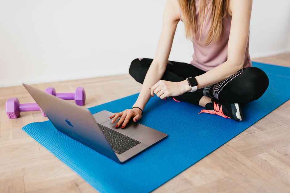 Mulher praticando exercícios em casa com um notebook, representando bem-estar e atividade física em um ambiente doméstico.