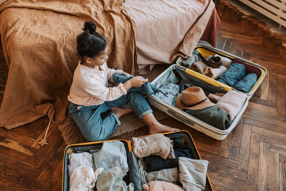 Menina organizando roupas para uma viagem enquanto se prepara para arrumar as malas em um ambiente doméstico aconchegante.
