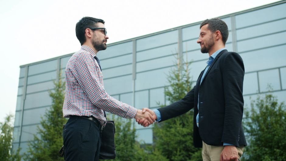 Duas pessoas se cumprimentando ao ar livre, simbolizando parceria ou fechamento de negócio em um ambiente corporativo.