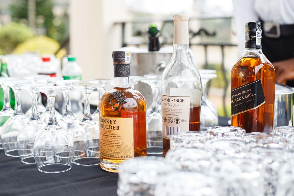 Imagem de uma mesa com garrafas de destilado e copos de degustação, sugerindo uma atmosfera de degustação ou evento de bebidas alcoólicas ao ar livre.