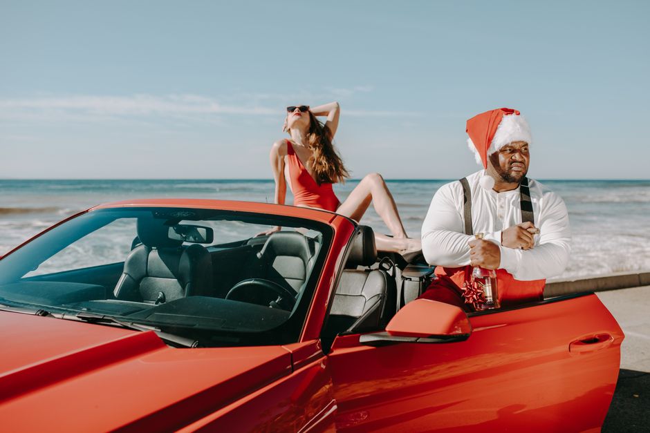 Mulher relaxando na praia ao lado de um homem com chapéu de Papai Noel, numa cena descontraída e festiva de fim de ano