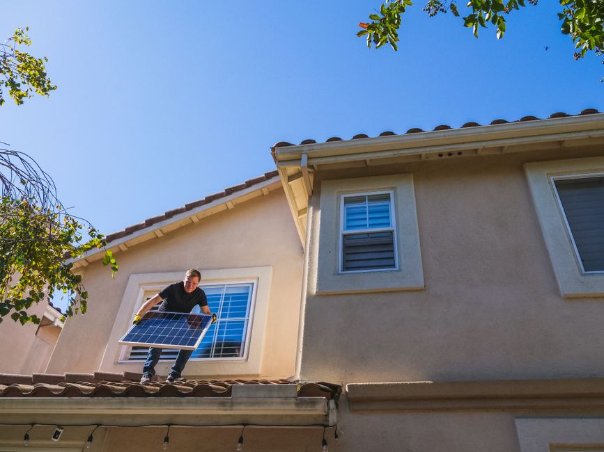 Homem instalando painéis solares em casa, representando energia sustentável e eficiência energética.