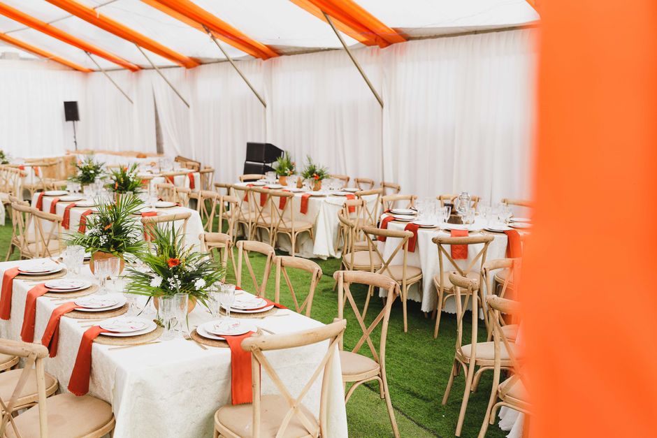 Imagem de um espaço para eventos ao ar livre, com mesas elegantemente decoradas e cadeiras de madeira, pronto para uma celebração ou refeição social.