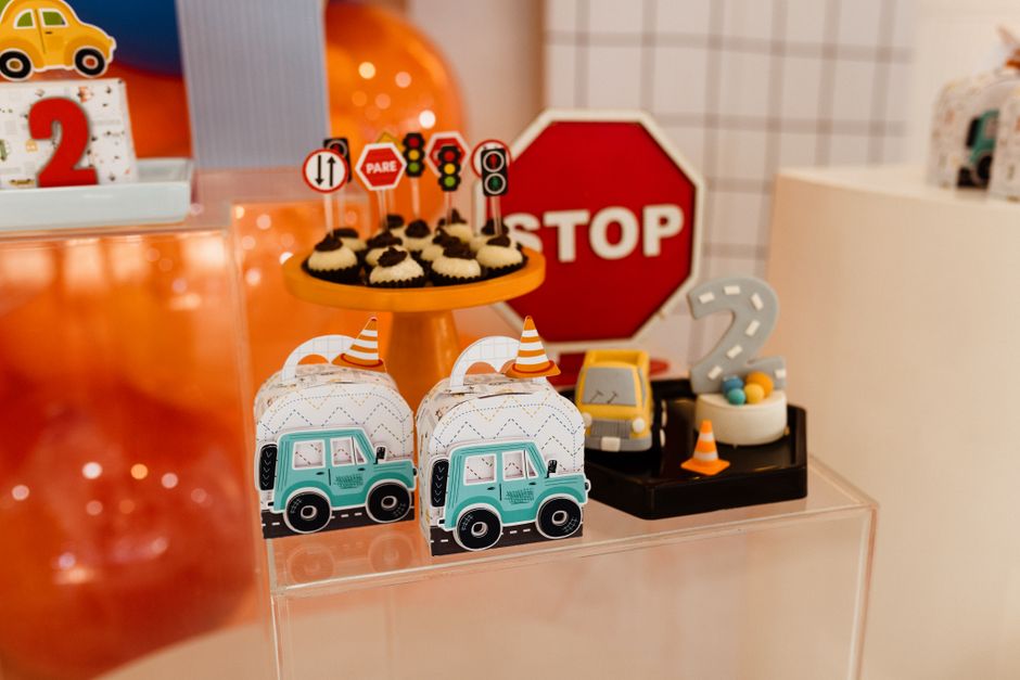 Imagem de uma festa infantil decorada com tema de trânsito, com miniaturas de carros, sinalizações e cupcakes decorados, criando um ambiente divertido e educativo.