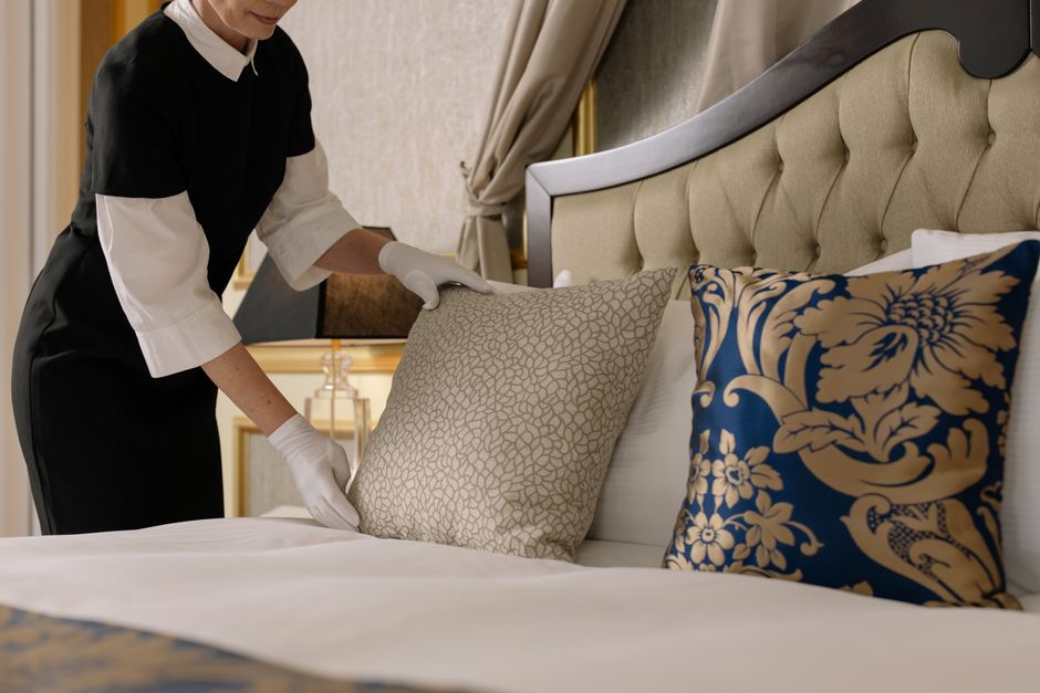 Profissional arrumando a cama em um ambiente de hotel de luxo, destacando a atenção aos detalhes na hospitalidade.