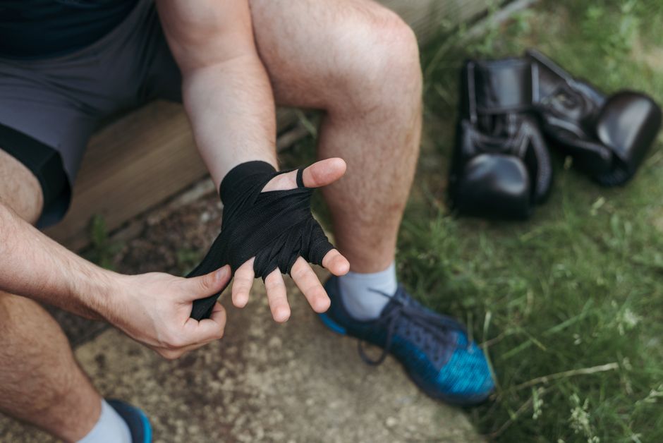 Homem ajustando uma bandagem de esportes no dedo em um ambiente ao ar livre, sugerindo cuidados com a saúde e atividades físicas ao ar livre.