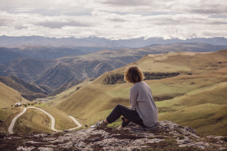 Mulher contemplando a paisagem de montanhas e vales verdes, refletindo sobre a conexão entre natureza e bem-estar.