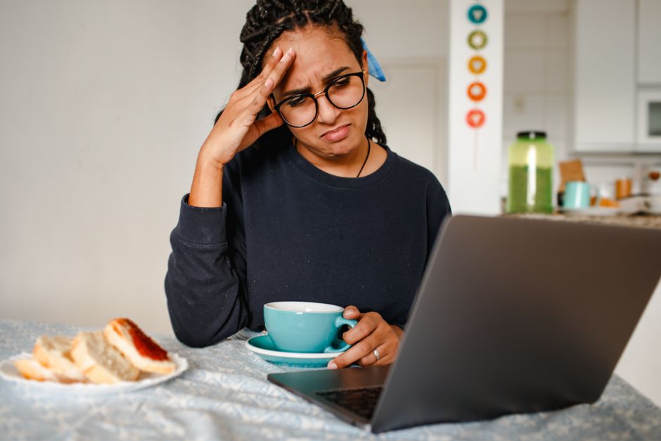 Mulher preocupada e estressada ao usar o computador em um ambiente doméstico, sugerindo temas de estresse ou dificuldades relacionadas ao trabalho ou estudos.