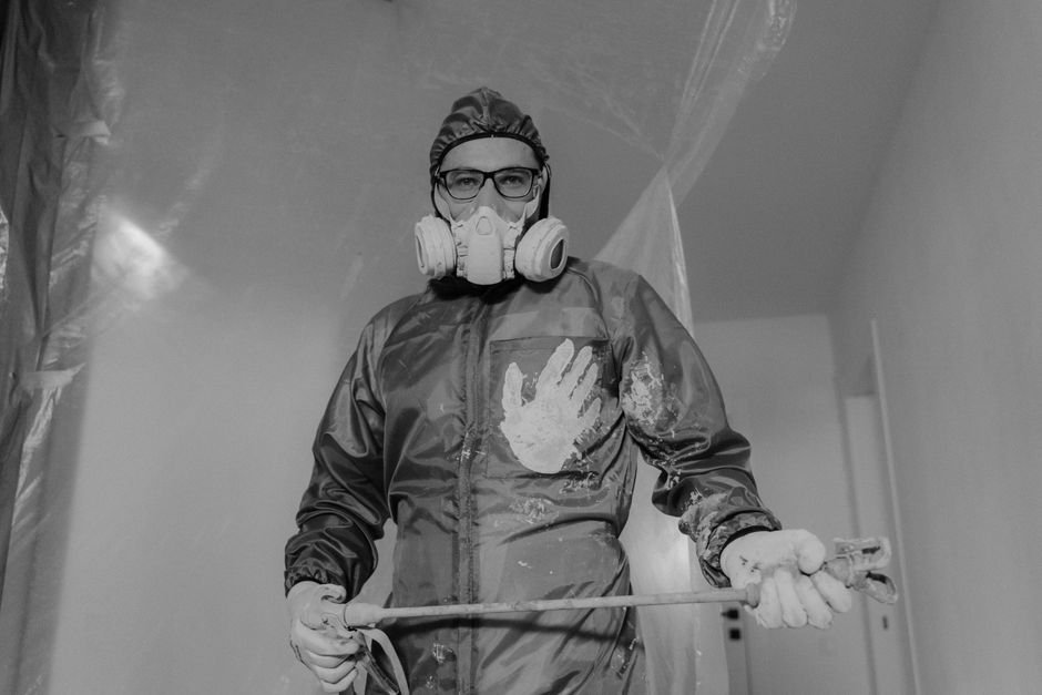 Profissional de saúde usando máscara de proteção e equipamentos de proteção individual durante procedimento na área da saúde, destacando a importância da segurança ocupacional.
