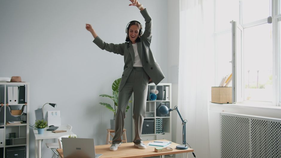 Mulher celebrando e dançando no escritório após sucesso ou conquista profissional, transmitindo alegria e realização.