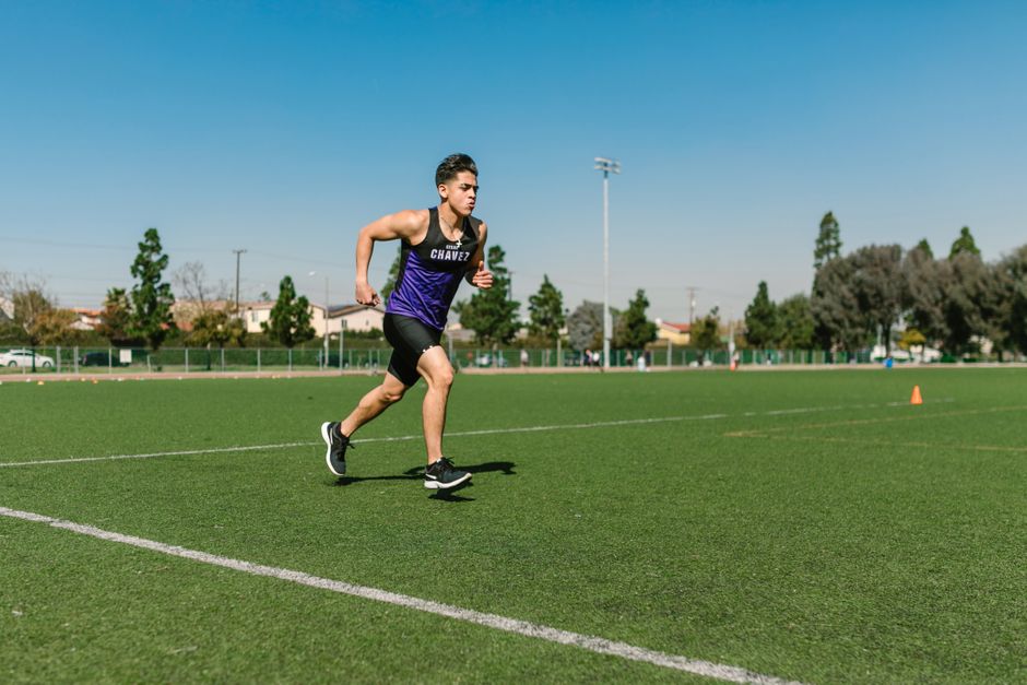 Atleta correndo em pista de grama ao ar livre durante treino ou competição.