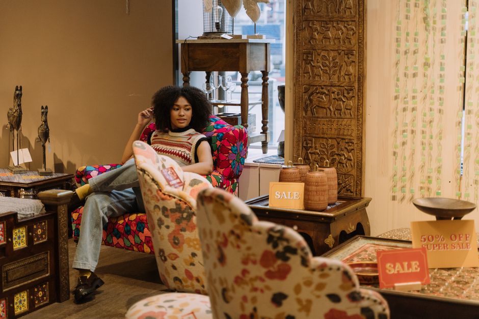 Mulher relaxando em um mobiliário com assento confortável em uma loja de móveis e decoração que exibe sinalizações de promoção e desconto.