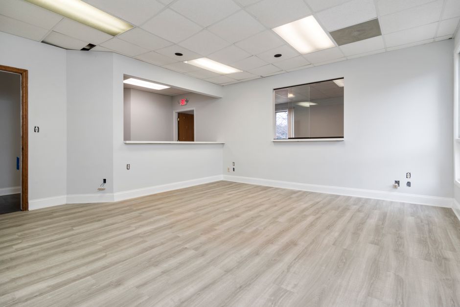 Imagem de um espaço de escritório vazio, com paredes brancas, piso de madeira clara e iluminação de teto, ideal para novos negócios ou ambientes corporativos.