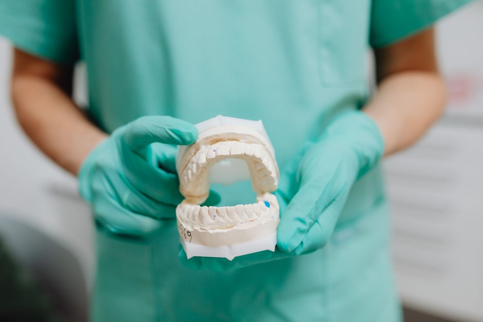 Profissional de odontologia segurando molde de dentes com preservativos, ilustrando cuidados bucais e prevenção em saúde oral.