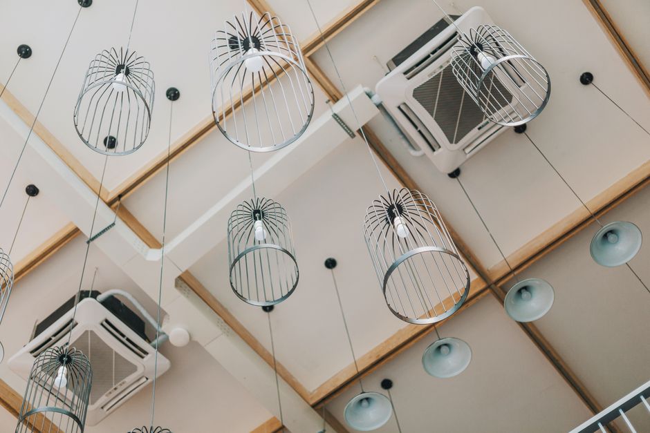 Imagem do teto de um espaço moderno com luminárias de design e aparelhos de ar-condicionado, ideal para ilustrar ambientes corporativos ou de coworking.
