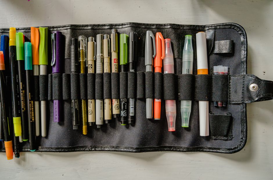 Imagem de um estojo aberto contendo várias canetas e marcadores coloridos, representando material de escritório ou itens de papelaria.