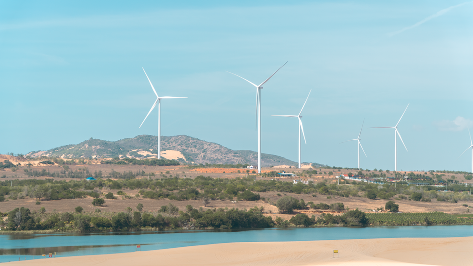 Paisagem de مناطmete de energia eólica com turbinas em um cenário de relevo ondulado e água ao fundo.