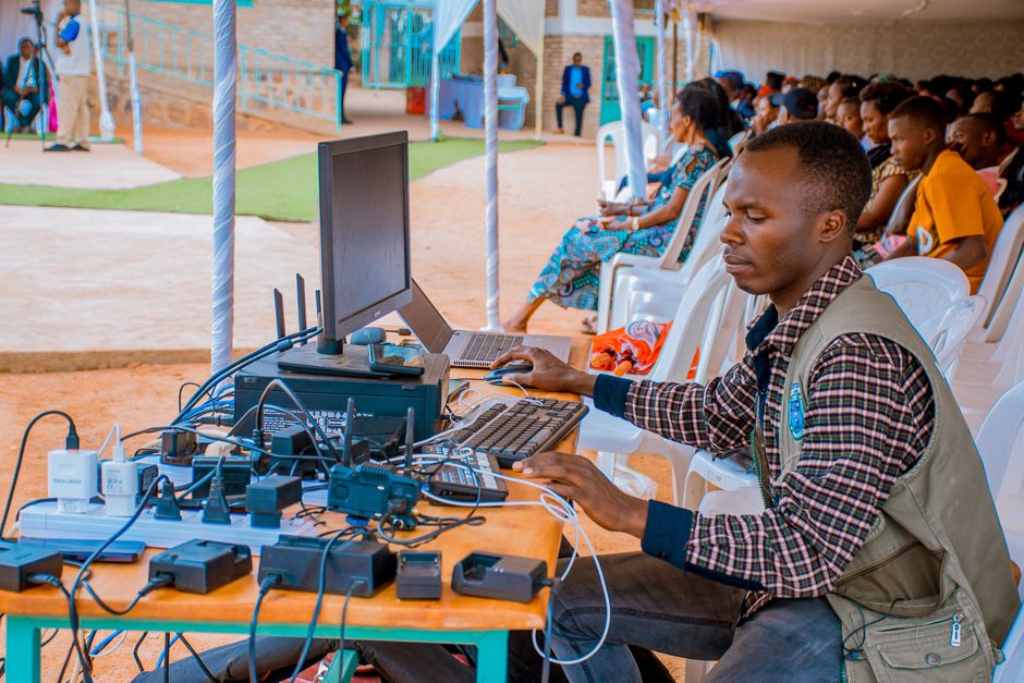 Homem utilizando equipamento de tecnologia para transmissão ao vivo em ambiente escolar ao ar livre, visando inclusão digital e educação.