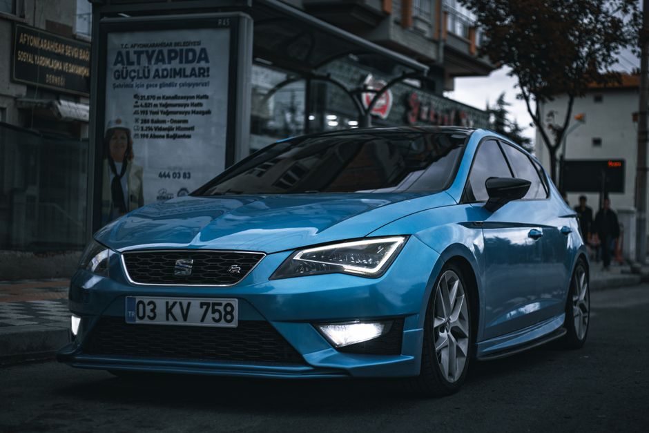Carro azul moderno estacionado na rua urbana durante o entardecer, refletindo a iluminação da cidade.