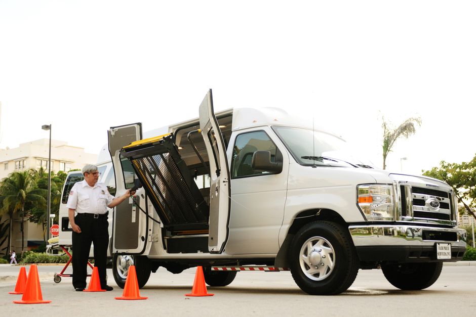 Veículo de transporte adaptado com equipamento de acessibilidade e uma pessoa realizando inspeção no local.